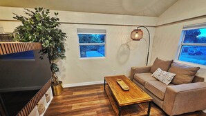 Una sala de estar con televisor, una mesa de centro de madera, un sofá y una planta grande.