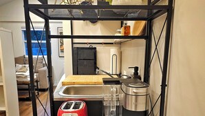 Un área de cocina con un estante metálico negro que contiene una tostadora roja, una cafetera, un hervidor y una cesta con objetos.