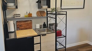 Cocina compacta con una paleta de colores blanco y negro, que incluye una encimera de madera, un lavamanos y un colgador para ollas.