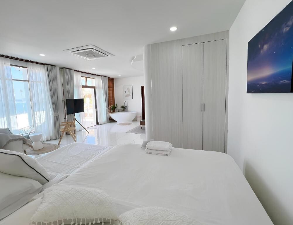 A modern bedroom with a large bed, a flat-screen TV, and a view of the outdoors through large windows.