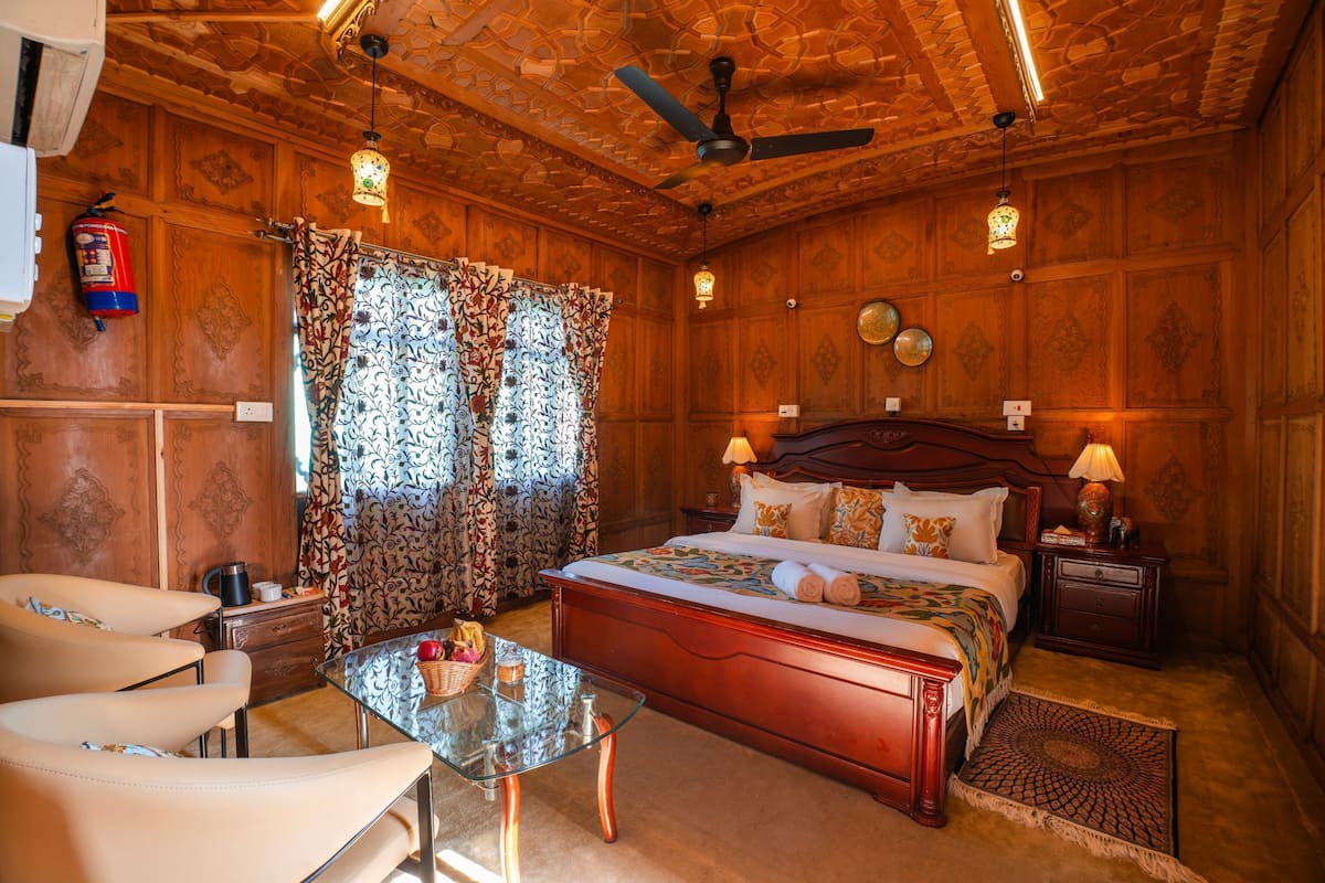 Quarto com painéis de madeira, uma cama, mesas de cabeceira, uma mesa de vidro e uma cadeira.