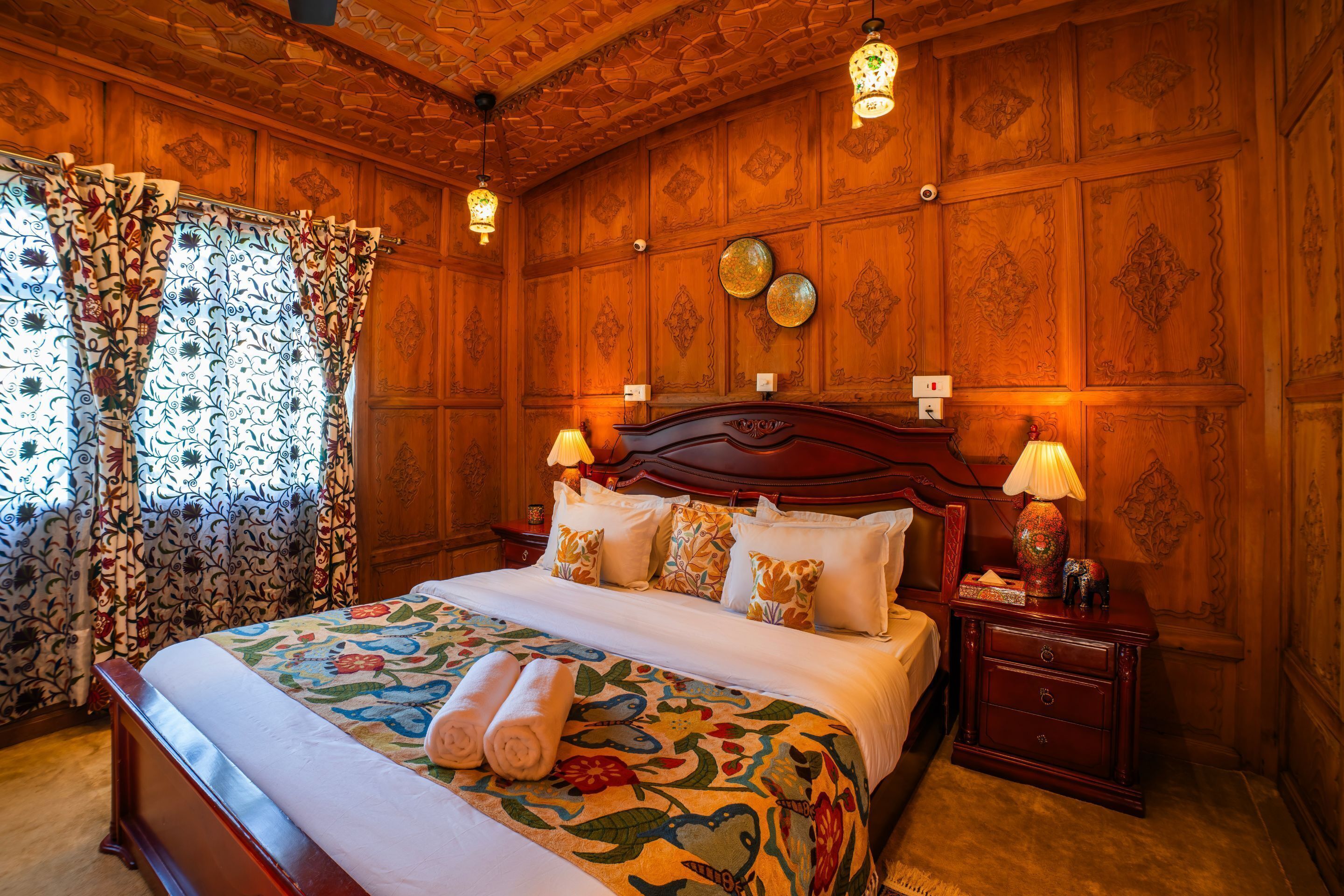 A traditional wooden room with a large bed, two bedside lamps, and patterned curtains.