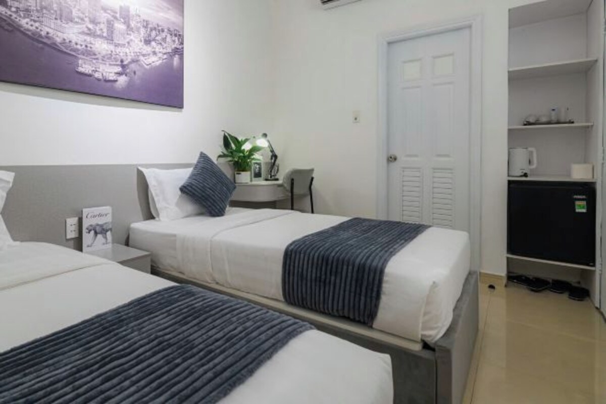 Una habitación de hotel con dos camas, un escritorio, una silla, una planta en maceta y un armario.