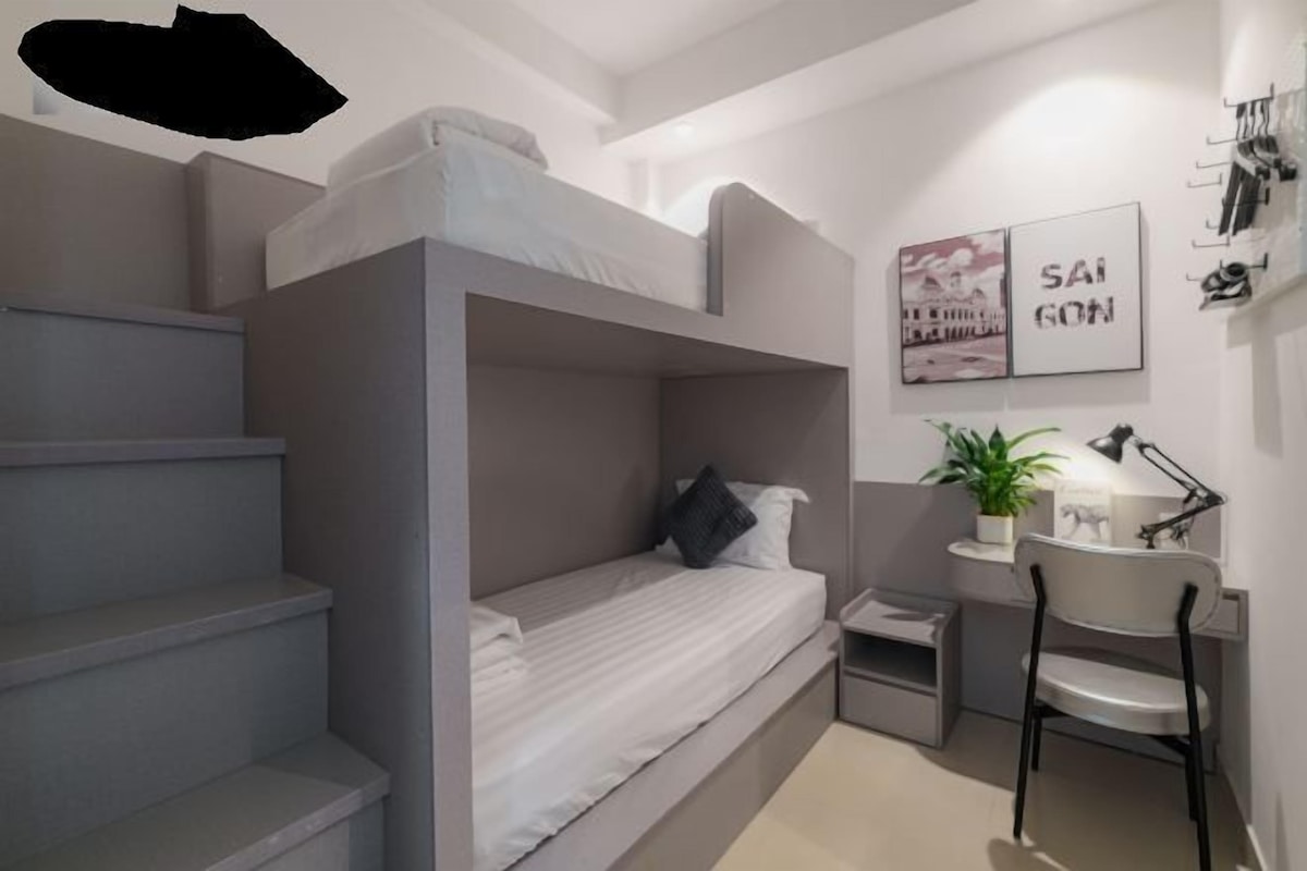 Habitación con literas, un escritorio, una silla, una planta pequeña y un estante en la pared.