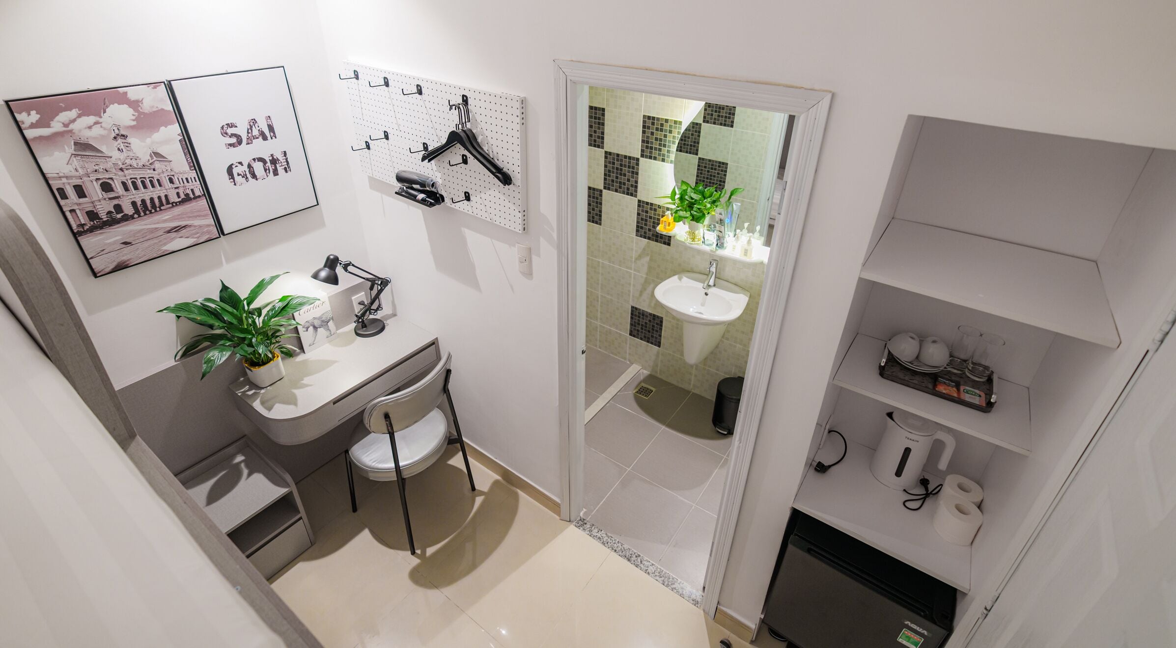 A compact bathroom with a sink, mirror, and toilet. There is a small plant on the counter and a shelf with toiletries.
