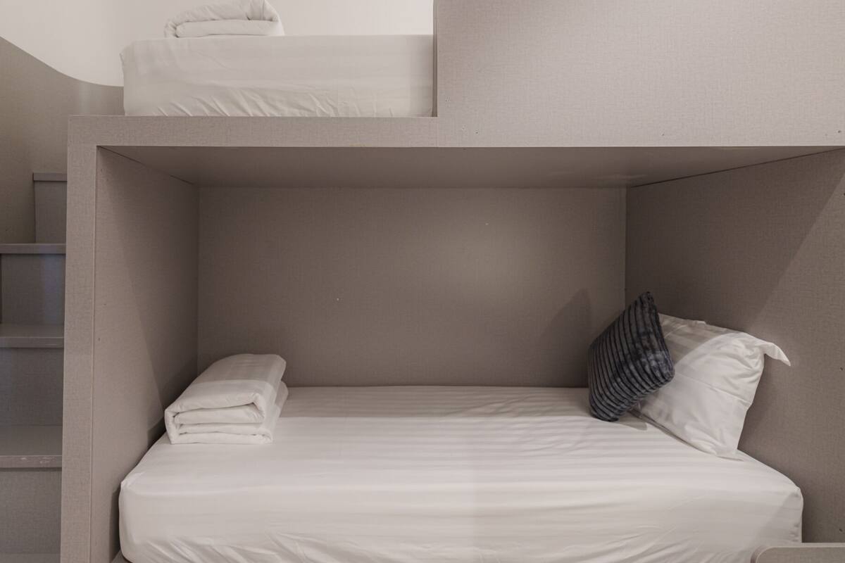 Un lit superposé avec un lit simple en dessous, un petit escalier et un mur uni.