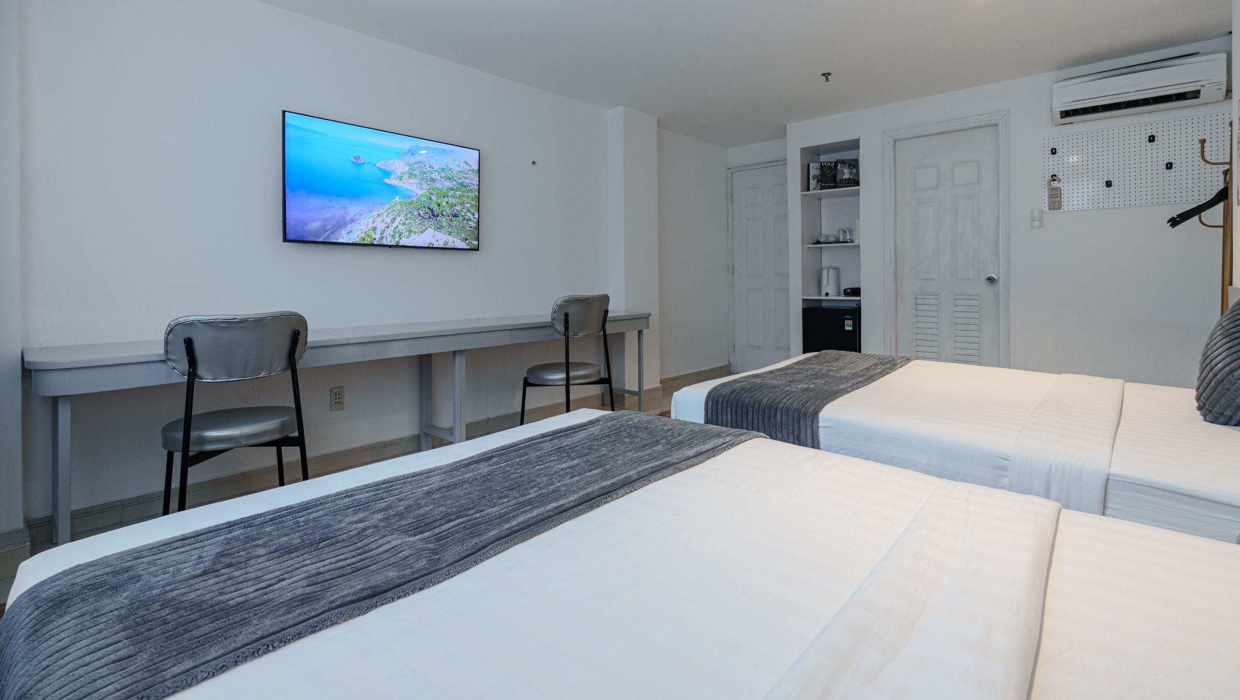 A hotel room with two beds, a desk with a chair, a television, and a wardrobe.