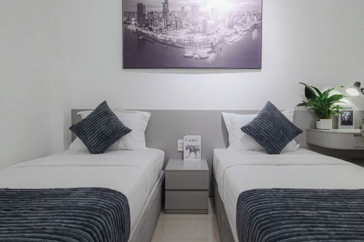 A hotel room with two beds, a nightstand, a framed picture of a cityscape, a small table with a plant, and a framed photo on the wall.