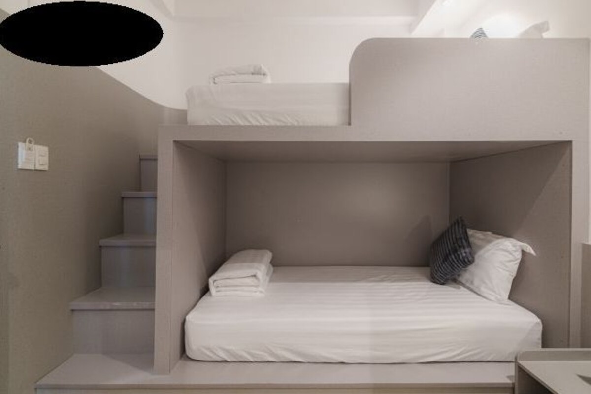 A bunk bed room with a white mattress, a folded white towel, and a striped pillow.