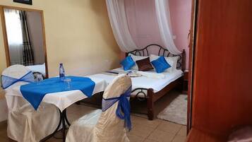 A room with a bed, a table, and a chair. There is a curtain over the bed and a picture on the wall.
