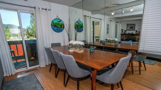 A dining area with a wooden table, grey upholstered chairs, and a large mirror reflecting the room. - Bayview Condo (Big Bear Lake)