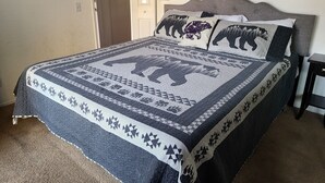 A bed with a quilt featuring a bear design, a headboard, and a nightstand with a lamp. - Bayview Condo (Big Bear Lake)