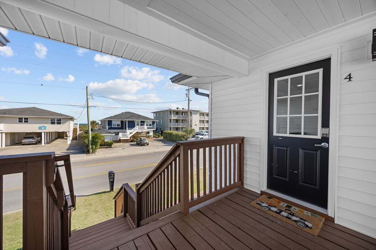 A porch with a black door, a wooden staircase, and a view of a street with buildings.