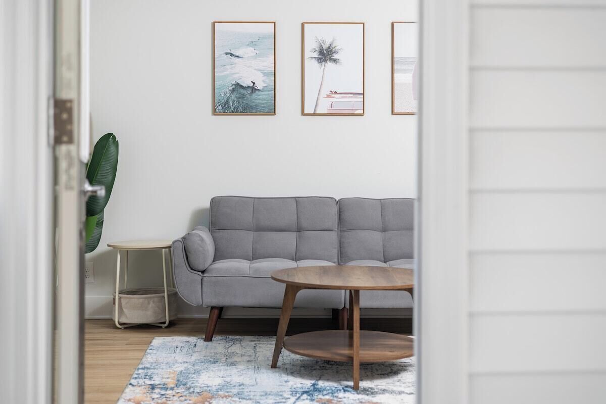 Un soggiorno con un divano grigio, un tavolino rotondo in legno e un tappeto decorato. Alle pareti, si vedono quadri incorniciati.