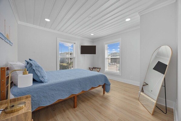 A bedroom with a bed, a desk, a chair, a TV, and a mirror.