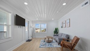 A modern living room with a flat-screen TV, a grey sofa, a wooden coffee table, and a brown leather chair. - Bright 2BR Surf Hideaway | 1-Min Walk to Waves (North Myrtle Beach)