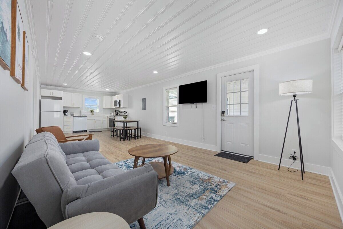 A modern living room with a gray sofa, a wooden coffee table, and a kitchen in the background.