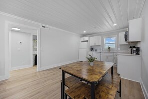A modern kitchen with white cabinets, a wooden dining table, and a window with blinds.