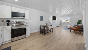 A modern kitchen with white cabinetry, stainless steel appliances, and a dining area with a wooden table and benches. - Bright 2BR Surf Hideaway | 1-Min Walk to Waves (North Myrtle Beach)