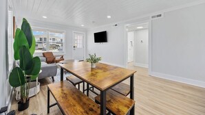 A modern interior with a wooden dining table, benches, a potted plant, and a flat-screen TV mounted on the wall. - 2BR Modern Surf Retreat | Steps to Sand (North Myrtle Beach)