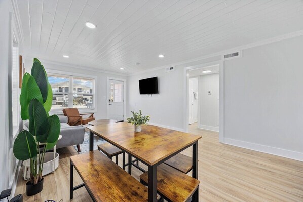 A modern interior with a wooden dining table, benches, a potted plant, and a flat-screen TV mounted on the wall.