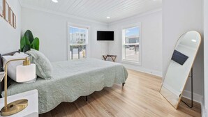 A bedroom with a bed, a TV, a mirror, and a window with a view. - 2BR Modern Surf Retreat | Steps to Sand (North Myrtle Beach)