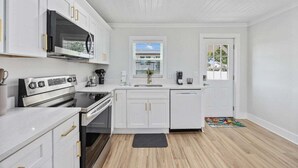 Una cocina moderna con armarios blancos, horno empotrado, microondas y cafetera.