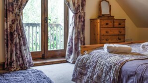 A bedroom with a large sliding glass door leading to a balcony, a wooden dresser, and a bed with a quilted cover. - 4 bedroom accommodation in Clifford, near Hay-on-wye (Clifford, near Hay-on-wye)