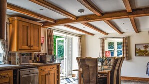 A kitchen with wooden cabinets, a microwave, and a dining area with a table and chairs. - 4 bedroom accommodation in Clifford, near Hay-on-wye (Clifford, near Hay-on-wye)