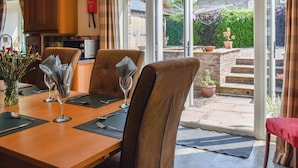 A dining area with a table set for four, chairs, a vase with flowers, and a view of the garden through glass doors. - 4 bedroom accommodation in Clifford, near Hay-on-wye (Clifford, near Hay-on-wye)