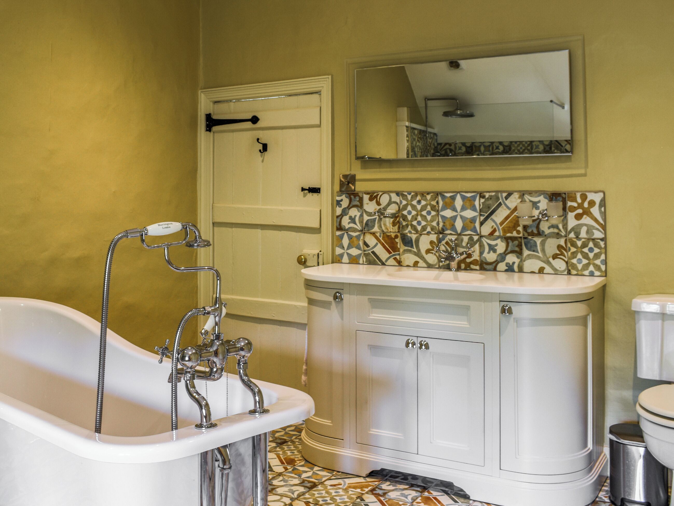 A bathroom with a freestanding bathtub, a sink with a decorative tile backsplash, and a toilet.