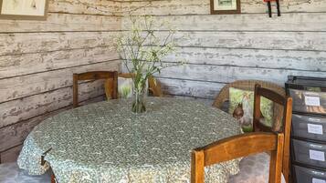 Een rustiek houten blokhutinterieur met een ronde tafel bedekt met een bloemrijk tafelkleed, omringd door houten stoelen.