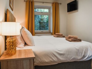 A hotel room with a bed, a bedside table with a lamp, a window with curtains, and a flat-screen TV mounted on the wall. - 3 Le Dorney Villa - UK49820 (Par)