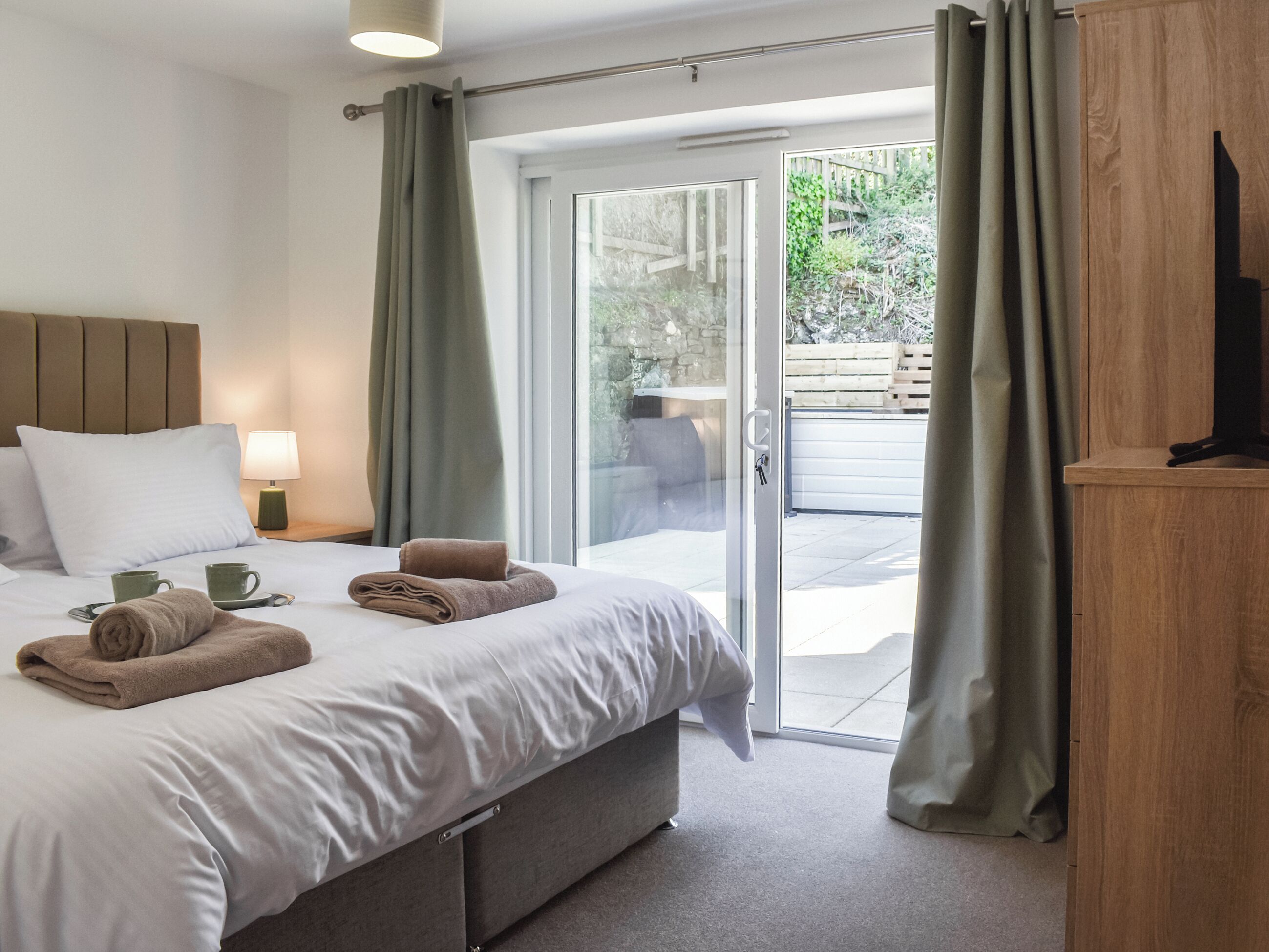 Une chambre d’hôtel comprenant un lit, une table de chevet, une lampe, un téléviseur et une porte-fenêtre coulissante donnant sur un espace extérieur.