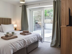 A hotel room with a bed, a nightstand, a lamp, a TV, and a sliding glass door leading to an outdoor area.