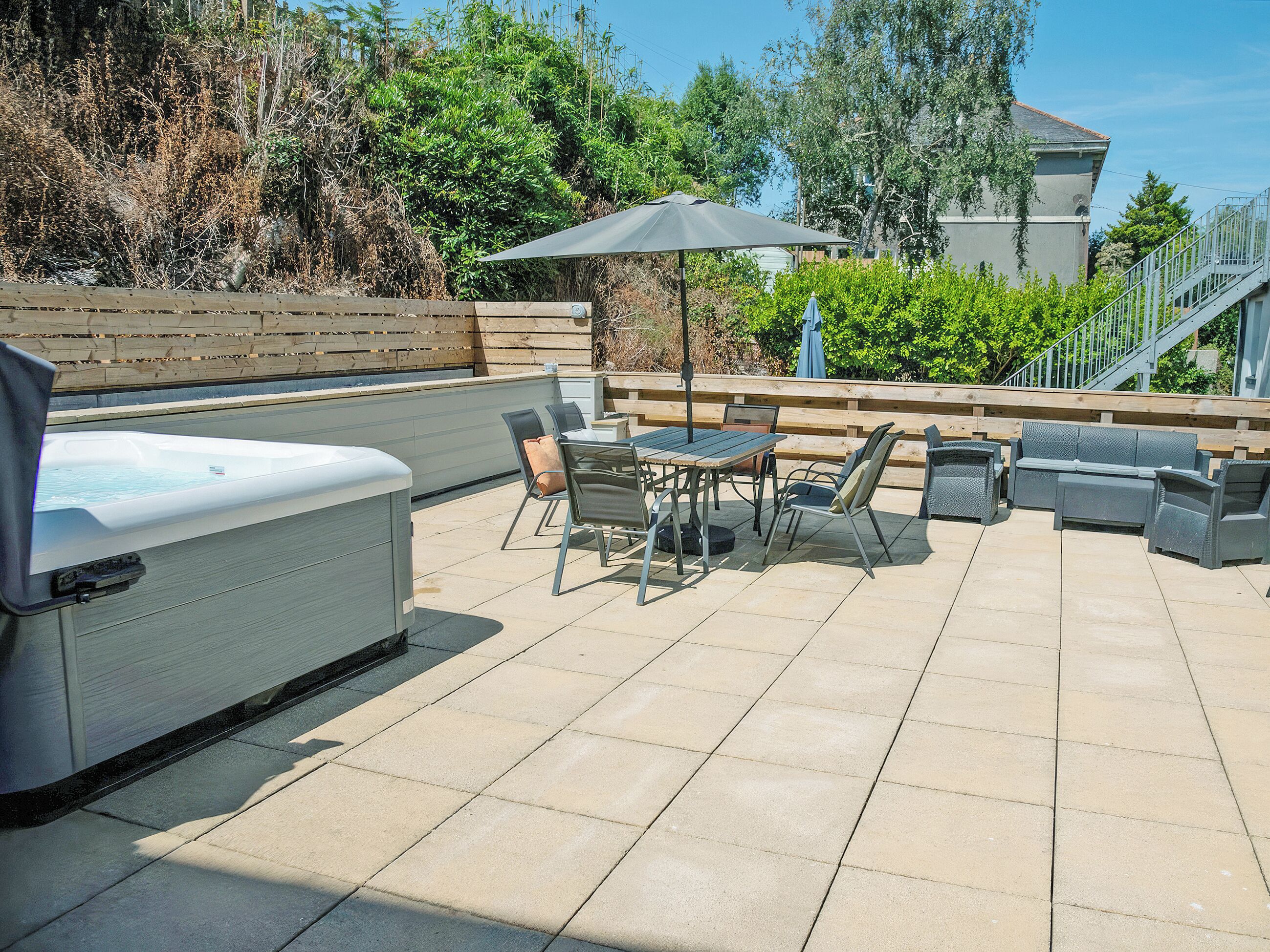An outdoor patio with a hot tub, seating area, and a wooden deck.