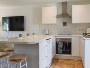A modern kitchen with white cabinetry, a built-in oven, and a flat-screen TV mounted above the counter.