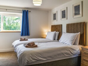 A double bed with white linens and a wooden headboard, a window with blue curtains, and three framed artworks on the wall.