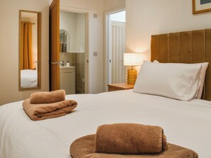 Une chambre d’hôtel avec un lit, une table de chevet, une lampe, un miroir et une salle de bain visible à travers une porte ouverte.