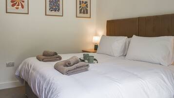 A neatly made bed with white linens, a brown headboard, and three framed abstract artworks on the wall.