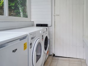 Une buanderie équipée d’un lave-linge et d’un sèche-linge blancs, d’une fenêtre et d’une porte blanche.
