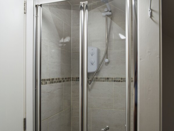 Un box de ducha con paredes de vidrio, un cabezal de ducha de mano y un panel de control en la pared.