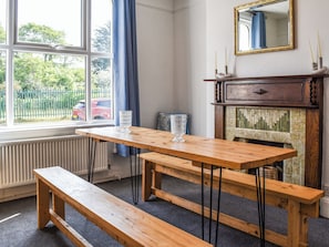 A room with a wooden table and bench, a fireplace, a window with curtains, and a mirror on the wall.