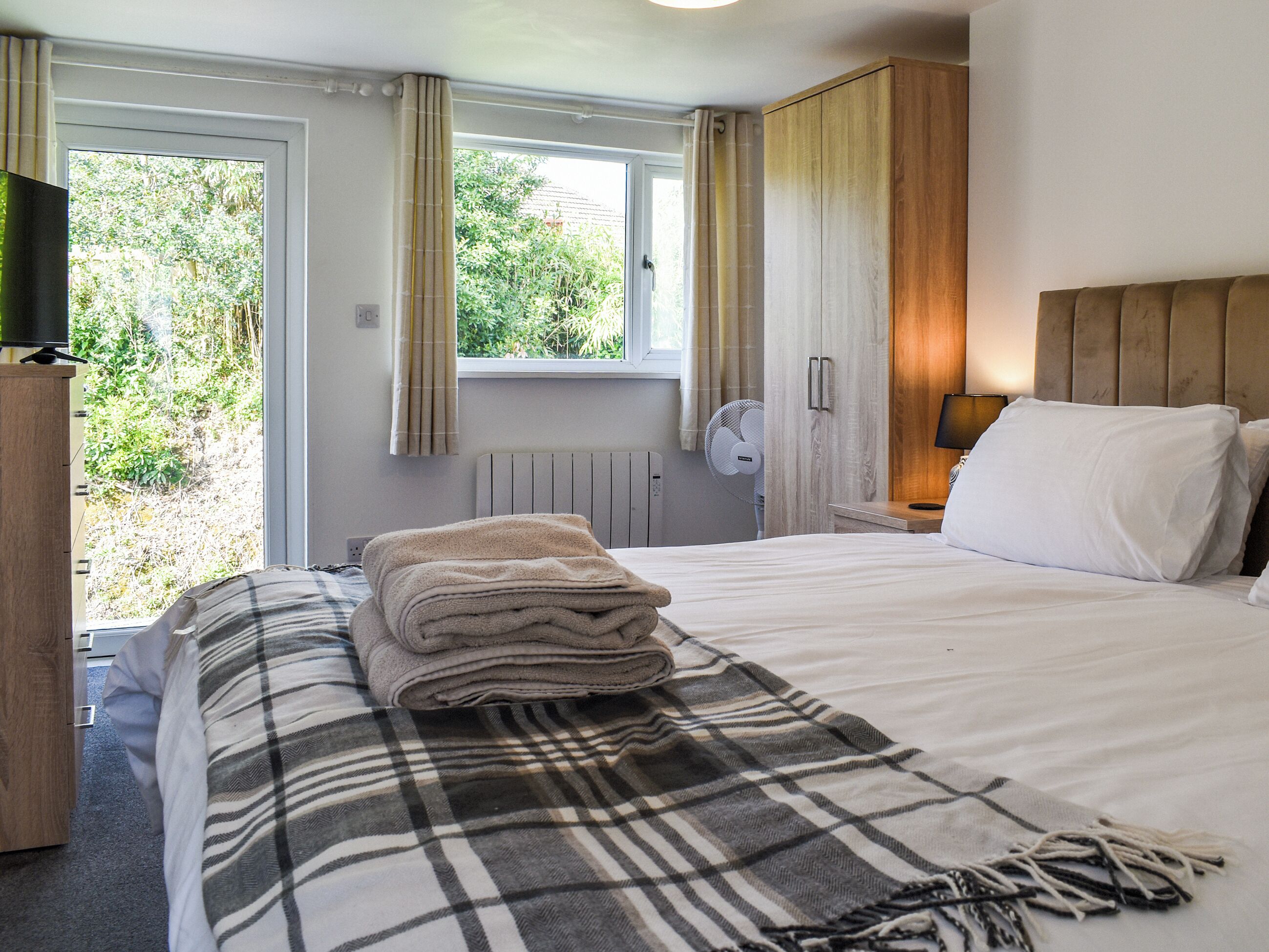 Una habitación de hotel con una cama, una mesita de noche, una lámpara, un ventilador y una ventana con cortinas.