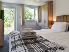 A hotel room with a bed, a bedside table, a lamp, a fan, and a window with curtains.