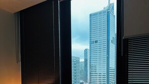A hotel room with a large window overlooking a cityscape, a bedside table with a lamp, and a bed with a green blanket. - 2 Bedroom Apartment near Southern Cross Station (Melbourne)