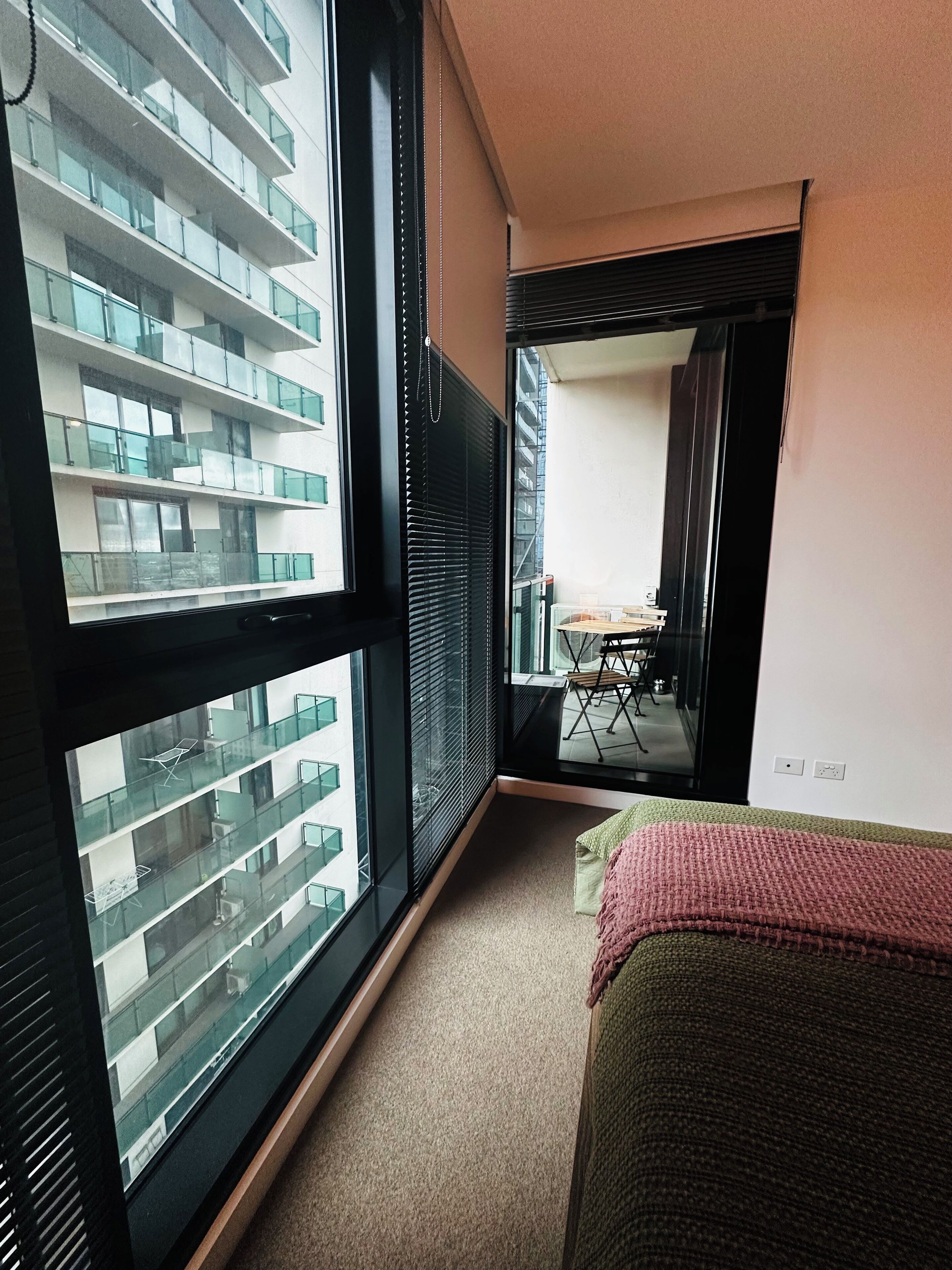 A narrow hallway with large windows, a view of a balcony with railings, and a glimpse of a dining area with a table and chairs.