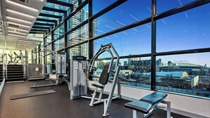A gym with exercise equipment and a bench, large windows with a city view, and a staircase leading to an upper level. - 2 Bedroom Apartment near Southern Cross Station (Melbourne)