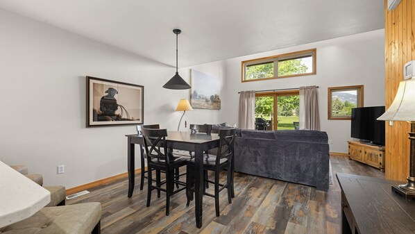 Una cocina moderna con comedor, piso de madera y ventanas amplias que dan vistas al exterior.