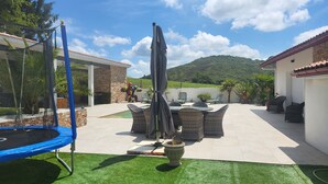 Un patio con mobili da esterno, un trampolino e vista su una collina.